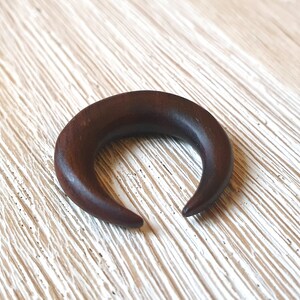 May include: A dark brown wooden crescent moon shaped ear gauge.