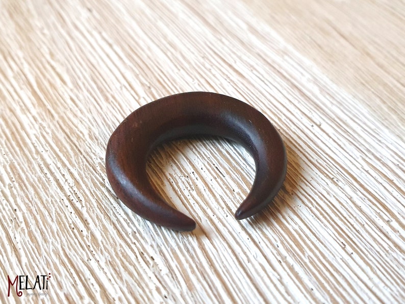 May include: A dark brown wooden crescent moon shaped ear gauge.