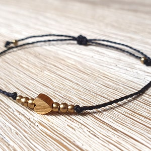 May include: A black string bracelet with a gold heart charm and gold beads.