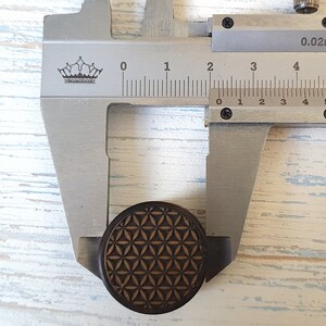 May include: A close-up of a wooden round plug with a geometric pattern, measured with a caliper. The caliper reads 0.02mm and shows a measurement of 2.5 cm.