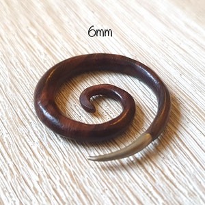 May include: A 6mm spiral wooden ear gauge with a silver metal spike. The gauge is made of dark brown wood with a natural grain pattern.