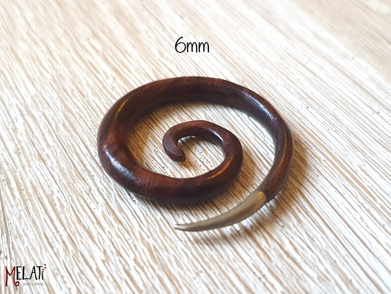 May include: A 6mm spiral wooden ear gauge with a silver metal spike. The gauge is made of dark brown wood with a natural grain pattern.