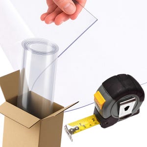 May include: A clear, rolled plastic sheet is partially unboxed, with a hand holding a flat piece. A black and yellow tape measure is in the foreground. The tape measure shows measurements in centimetres.