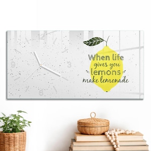 May include: A rectangular wall clock with a white speckled background. The left side features a clock face with white hands and numbers. The right side displays a yellow lemon illustration with the text When life gives you lemons make lemonade.