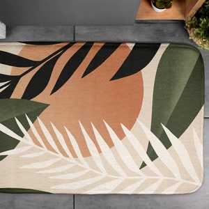 Puede incluir: Una alfombra de baño beige con un diseño abstracto moderno con hojas blancas, negras, verdes y naranjas.