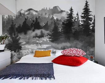 Op de afbeelding: Een wit bed met een grijs deken en rode, witte en gele kussens. De muur achter het bed heeft een zwart-wit aquarel schilderij van een bos.
