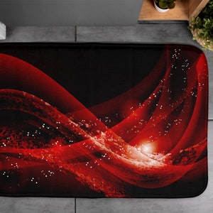 Peut inclure: Tapis de bain rectangulaire avec un fond noir et un motif abstrait rouge dynamique. Le motif présente des lignes ondulées et des points blancs épars, créant une sensation de mouvement et de profondeur. Le tapis est probablement en matière douce et absorbante.