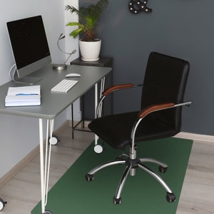 Può includere: Un ufficio con una scrivania grigia con computer, tastiera e mouse. Una sedia da ufficio in pelle nera con braccioli in legno è su un tappetino verde. Sono visibili anche una pianta in vaso e una lampada da scrivania.