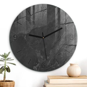 May include: A circular wall clock featuring a dark charcoal gray marble pattern with white veining. The clock face displays black hour and minute hands, a thin second hand, and black numerals at the 3, 6, 9, and 12 o'clock positions.