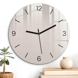 Puede incluir: Un reloj de pared redondo con una esfera de color beige claro lisa que presenta números negros en las posiciones de las 12, 3, 6 y 9. El reloj tiene manecillas negras finas para las horas y minutos, un segundero negro y marcas negras.