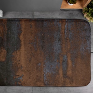 Peut inclure: Un tapis de bain abstrait à motifs marrons et bleus. Le tapis a une surface texturée et est conçu pour absorber l'eau.