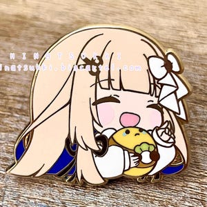 May include: Gold-colored enamel pin featuring a cartoon character with long blonde hair, wearing a blue and white outfit, holding a yellow and green food item. The character has a happy expression with closed eyes and a wide smile. The pin has a shiny finish and is designed in a cute and whimsical style.