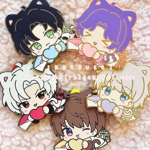 Puede incluir: Colección de cinco pines de esmalte con personajes de estilo anime con orejas de gato. Cada pin muestra un personaje sosteniendo un corazón y un sobre. Los pines tienen varios colores de cabello, con detalles dorados.