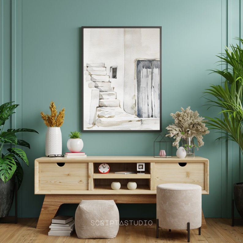 May include: A watercolor painting of a white building with a doorway and steps, framed in black and hanging on a teal wall above a wooden media console with two drawers and two shelves. The console is decorated with a clock, two white candles, and a potted plant. Two gray ottomans are in front of the console.