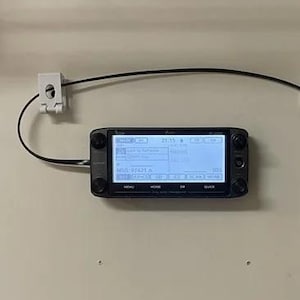 May include: A wall-mounted electronics setup featuring a black display screen, a black box, and a handheld microphone. Wires and connectors are visible, indicating a communication or data system.