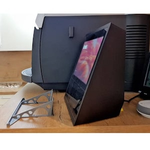 May include: A black Echo Show smart display with a screen showing a photo of a beach. The display is on a wooden surface with a metal stand.