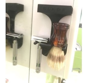 May include: A black plastic holder with a razor and a shaving brush. The shaving brush has a brown wooden handle and a white brush head.