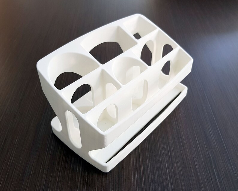 May include: White plastic organizer with multiple compartments, designed for storing small items. The organizer has a tiered design with a lower shelf and a top section with several open slots.
