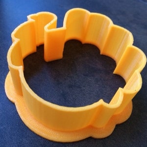 May include: A yellow plastic cookie cutter shaped like a flower with a scalloped edge.
