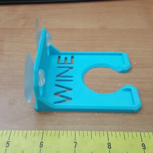 May include: A blue plastic wine bottle holder with suction cups. The holder has the word "WINE" cut out of the front.