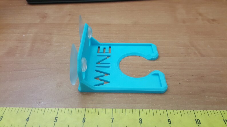 May include: A blue plastic wine bottle holder with suction cups. The holder has the word "WINE" cut out of the front.