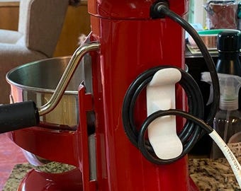 May include: A close-up of a red KitchenAid stand mixer. The mixer has a stainless steel bowl and a black power cord. The text "U.S.A. 1 (800) 541 6390" and "CANADA 1 (800) 461 5681" is visible on the mixer.