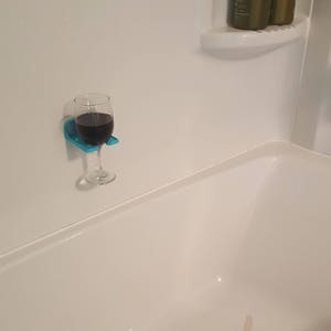 May include: A blue glass holder with a glass of red wine attached to a white tiled shower wall.