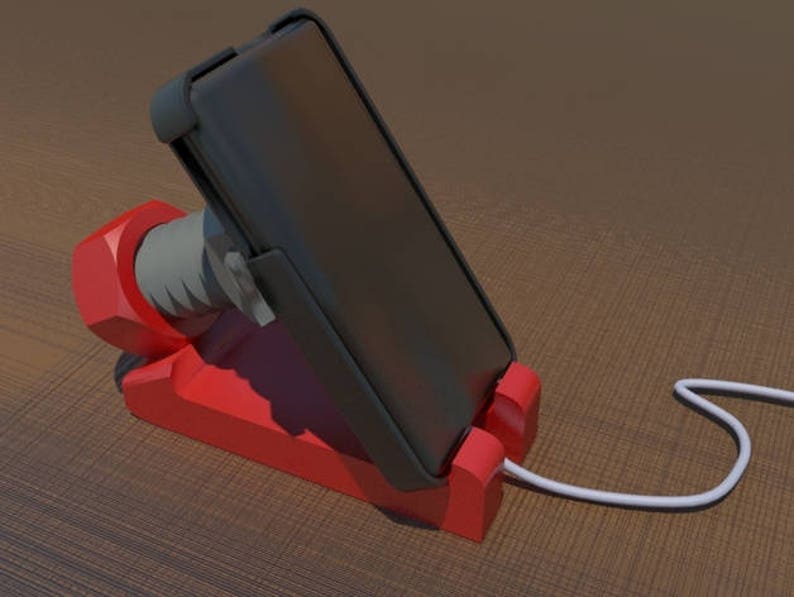 May include: A red phone stand with a black phone in a vertical position. The phone is connected to a white charging cable.