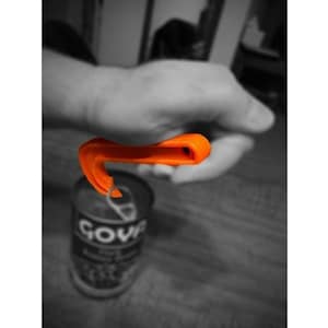 Peut inclure: Outil d'ouverture de boîte de conserve en plastique orange avec une poignée incurvée. L'outil est utilisé pour ouvrir une boîte de soupe.