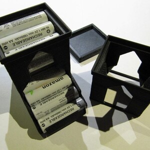 May include: A black plastic battery storage container with a clear plastic window. The container holds four rechargeable AA batteries. The batteries are labeled "RECHARGEABLE Ni-MH 1.2V min. 1900mAh AA HR6" and "amazon".