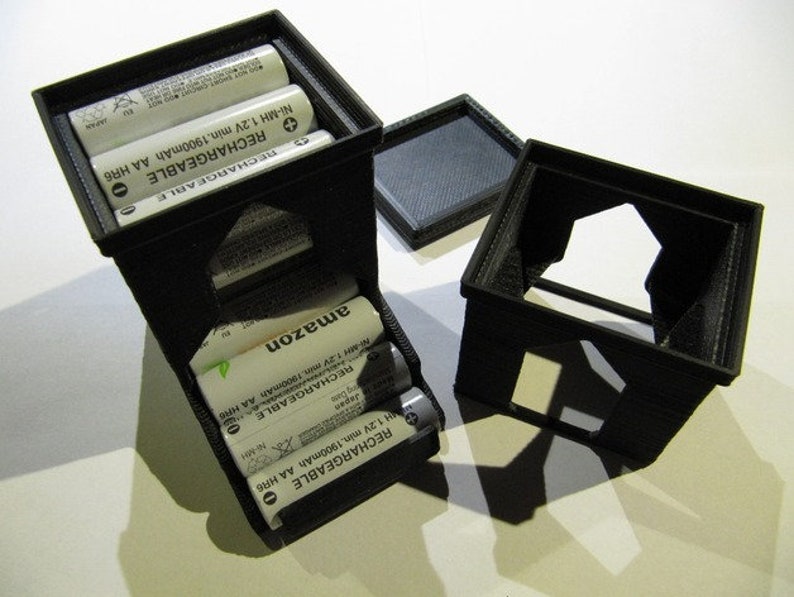 May include: A black plastic battery storage container with a clear plastic window. The container holds four rechargeable AA batteries. The batteries are labeled "RECHARGEABLE Ni-MH 1.2V min. 1900mAh AA HR6" and "amazon".
