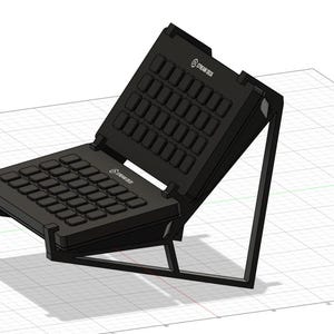 Może przedstawiać: Czarny Stream Deck z wieloma przyciskami, ustawiony pod kątem na stojaku. Na Stream Decku widnieje napis "Stream Deck". Stojak jest czarny i ma geometryczny kształt.