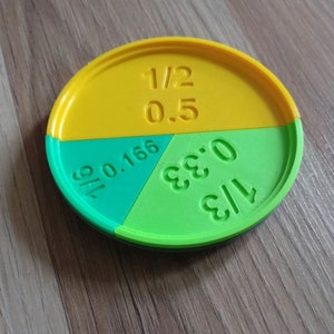 Puede incluir: Una herramienta de enseñanza circular amarilla, verde y negra con fracciones y decimales escritos en ella. Las fracciones son 1/2, 1/3 y 1/6. Los decimales son 0,5, 0,33 y 0,166.