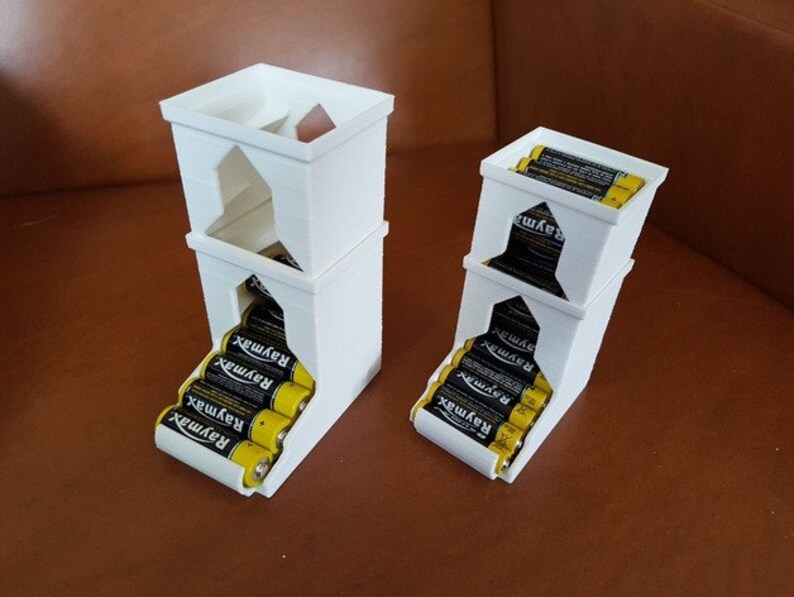 May include: Two white 3D printed battery organizers. The larger organizer is stacked three levels high and holds 6 AA batteries. The smaller organizer is stacked two levels high and holds 4 AA batteries. Both organizers have a slot for the batteries to slide into.
