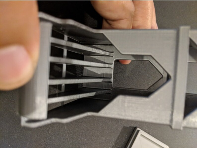 May include: A 3D printed gray plastic object with a series of parallel slots and a rectangular opening.