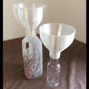 May include: Two clear plastic funnels, one attached to a repurposed plastic jug and the other to a clear bottle. The funnels have a wide, flared top and a narrow spout. The jug contains colorful beads.