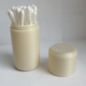 May include: A white plastic container with a textured surface, filled with cotton swabs. The container has a separate lid with a textured surface.