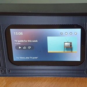 以下が含まれることがあります： スマートデバイスにデジタルテレビガイドが表示された、黒色の3Dプリントされたビンテージテレビのレプリカ。画面には13:08の時間と「今週のテレビガイド」というテキストが表示されています。