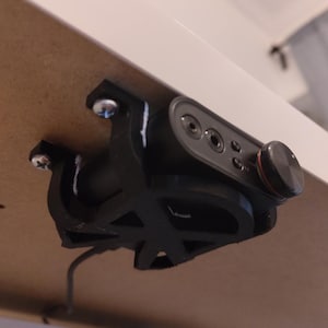 May include: A black audio interface device with a volume knob and multiple input/output jacks is mounted under a white surface. The device is attached with a black bracket and silver screws. A cable extends from the device.