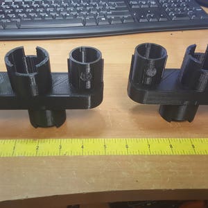 May include: Two black 3D printed organizers with multiple slots for holding items. The organizers are on a wooden surface with a yellow ruler.