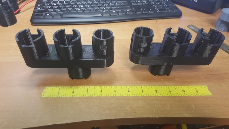 May include: Two black 3D printed organizers with multiple slots for holding items. The organizers are on a wooden surface with a yellow ruler.