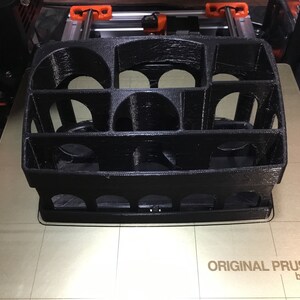 May include: A black 3D printed object with a grid-like design. The object is sitting on a beige surface with the text "ORIGINAL PRUSA i3 MK3 by Josef Prusa" printed on it.