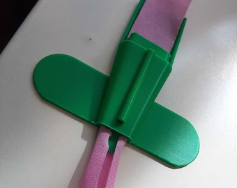 Op de afbeelding: Een groene plastic lint houder met een roze lint erdoorheen.