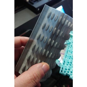 May include: A close-up of a grey 3D printed object with a textured surface. The object has a series of small, raised bumps in a repeating pattern.