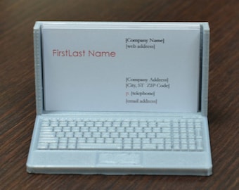 Könnte beinhalten: Ein weißer 3D-gedruckter Laptop-Visitenkartenhalter mit einer weißen Visitenkarte im Inneren. Die Visitenkarte trägt den Text "FirstLast Name" und die Kontaktdaten eines Unternehmens.
