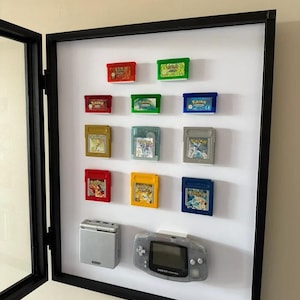 以下が含まれることがあります： ゲームボーイアドバンスのカートリッジと2つの携帯ゲーム機を収めた額入りのディスプレイ。カートリッジは赤、緑、青、黄色など様々な色があります。コンソールはシルバーとグレーです。