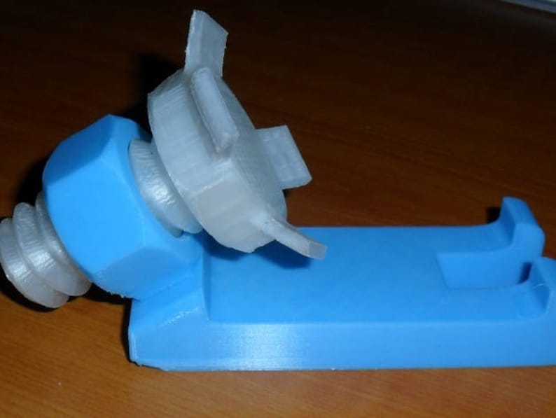 May include: A 3D printed phone stand with a blue base and a white, adjustable phone holder. The holder is shaped like a nut and bolt.