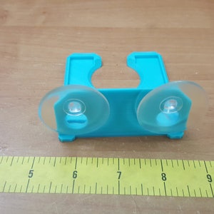 May include: A turquoise plastic shower caddy with two suction cups. The caddy is designed to hold shampoo bottles or other bathroom items.