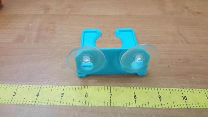 May include: A turquoise plastic shower caddy with two suction cups. The caddy is designed to hold shampoo bottles or other bathroom items.