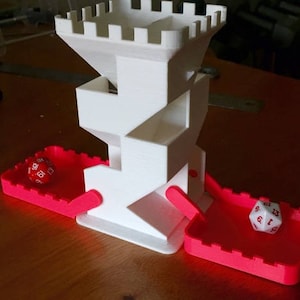 May include: A white 3D-printed dice tower with a castle-like design. Two red trays are attached to the tower, each holding a die. One die is red, the other is white. The tower is on a wooden surface.